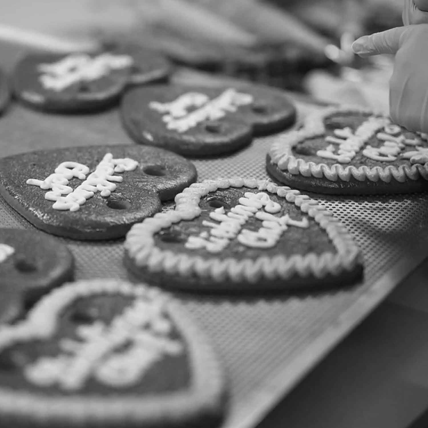 Liebeskekse mit Zuckerglasur auf einem Backblech, ein Herz wird individuell verziert.