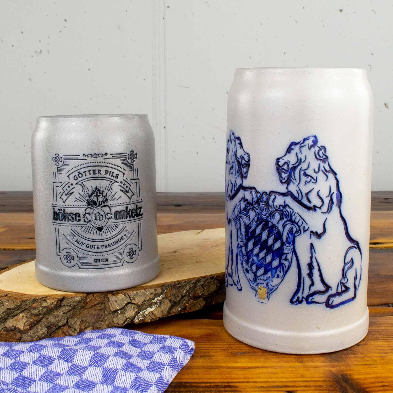 Zwei Keramik-Bierkrüge: einer mit schwarzer Aufschrift "Götter Pils" und einer mit bayerischem Wappen und blauen Löwen.