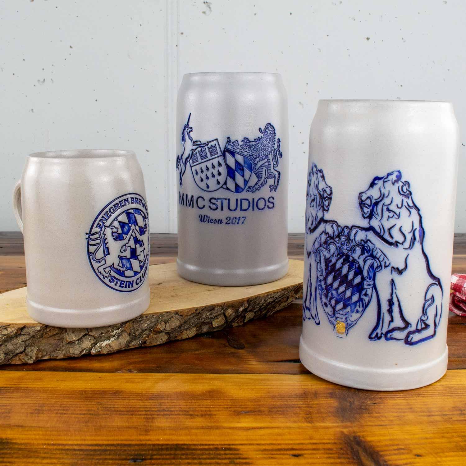 Drei Bierkrüge aus Steingut, hellgrau, mit individuellen blauen Wappen- und Löwenmotiven auf rustikalem Holztisch.
