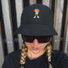 Frau mit Zöpfen und Sonnenbrille trägt schwarzen Pumuckl Fischerhut mit "Grantla" Motiv Stickerei.