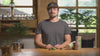 Junger Mann mit Bart und Käppi zeigt Pellets zum Pflanzen für natürliches Wachstum im Video.