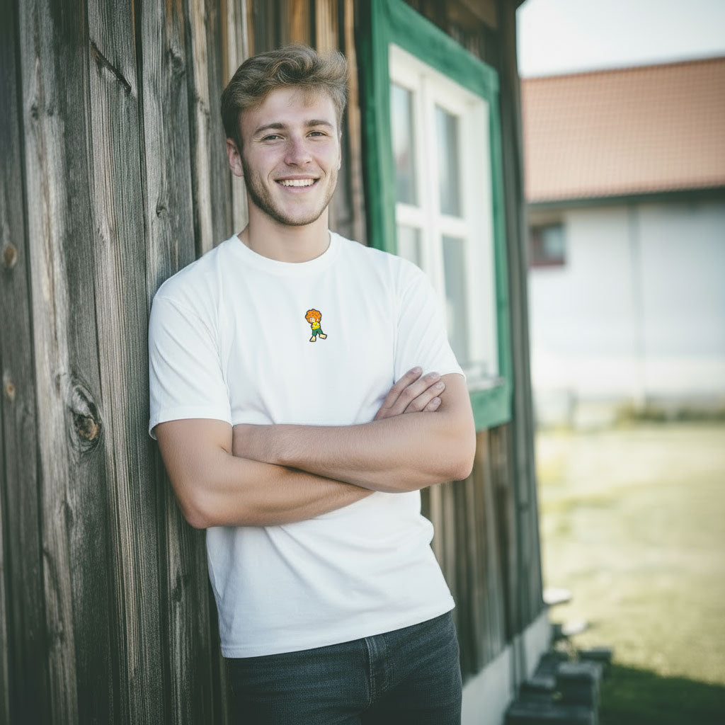 Lächelnder Mann in weißem Pumuckl Herren T-Shirt "Grantla" mit kleinem Pumuckl-Motiv; lehnt an Holzwand.