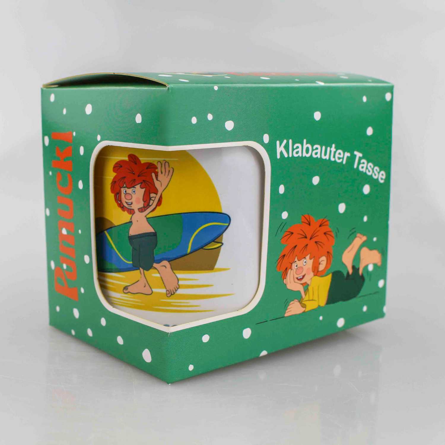 Pumuckl Tasse mit Surfer-Motiv auf grünem Geschenkkarton, Klabauter Figur mit Surfbrett am Strand.
