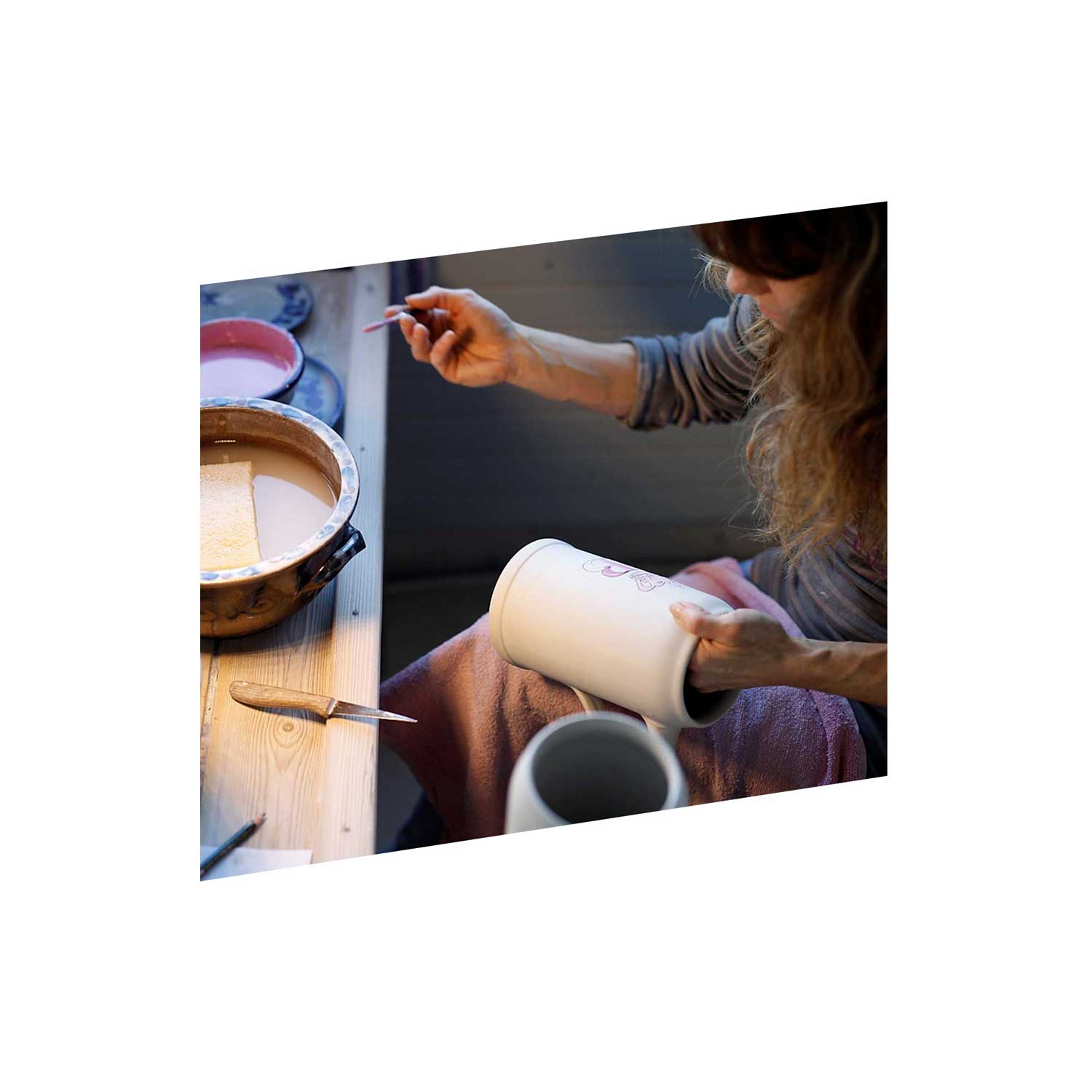 Künstlerin bemalt traditionellen weißen Keramik-Bierkrug von Hand mit feinem Pinsel und rosa Farbe.