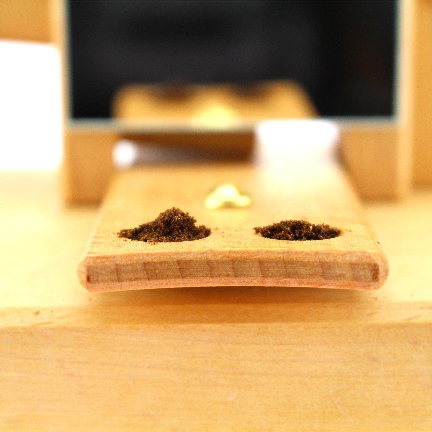 Holzschieber mit zwei Portionen brauner Tabakspulver in Aussparungen, bereit zur Verwendung.